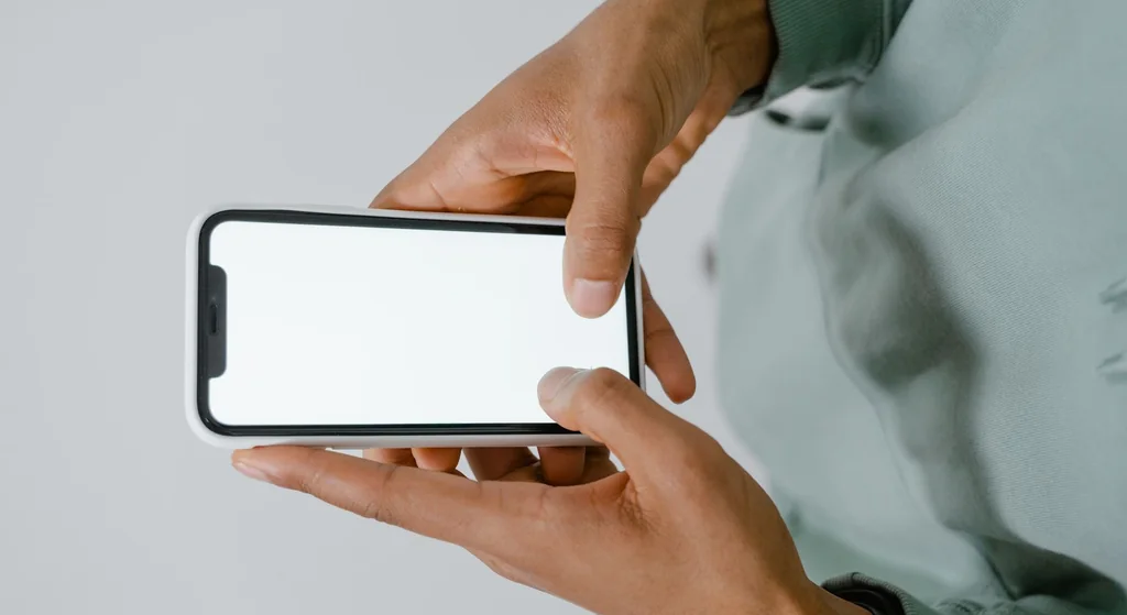 Stock photograph: two hands holding a smartphone with a blank screen, held horizontally in front of a plain background