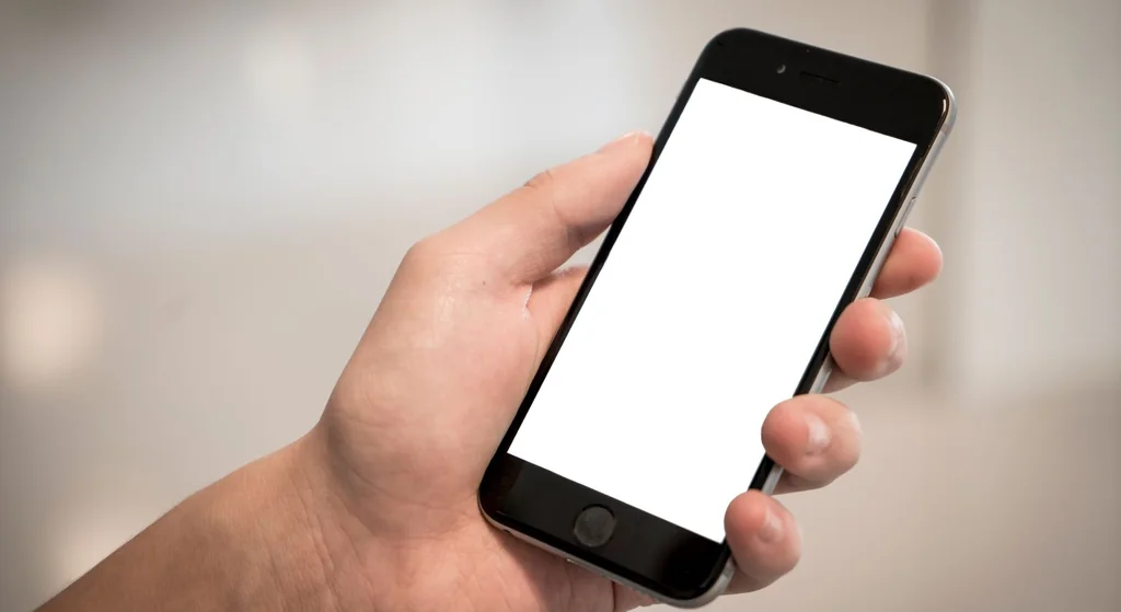 Stock photograph: a hand holding a smartphone with a blank screen, against a softly blurred indoor background